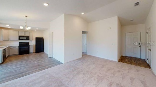 kitchen with decorative light fixtures, light colored carpet, lofted ceiling, and black appliances