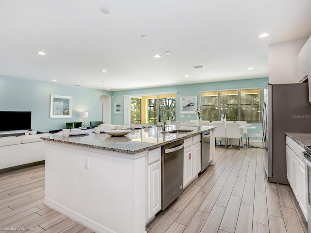 kitchen with light stone countertops, appliances with stainless steel finishes, sink, a center island with sink, and white cabinets