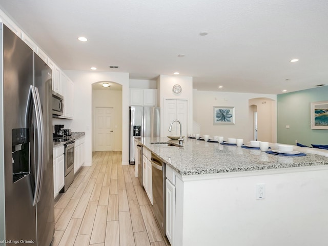 kitchen featuring white cabinetry, sink, a large island, stainless steel appliances, and light stone counters