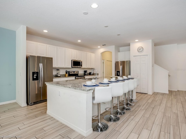 kitchen with light stone countertops, stainless steel appliances, a breakfast bar area, a center island with sink, and white cabinets