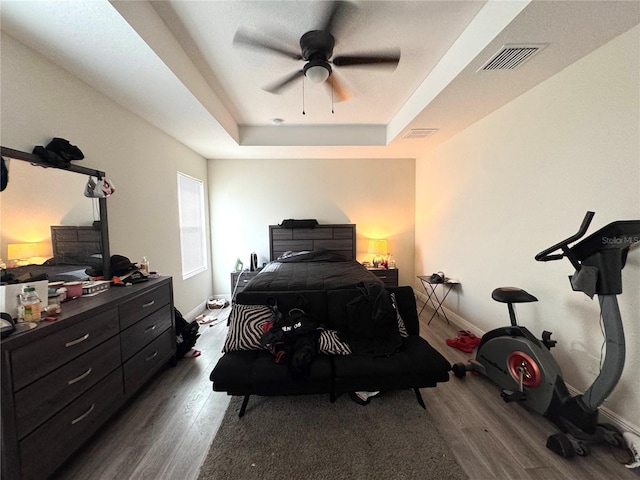 bedroom with dark hardwood / wood-style flooring, a tray ceiling, and ceiling fan