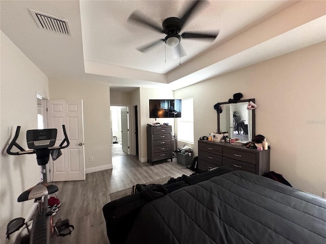 bedroom with ceiling fan, a textured ceiling, a tray ceiling, and light hardwood / wood-style flooring