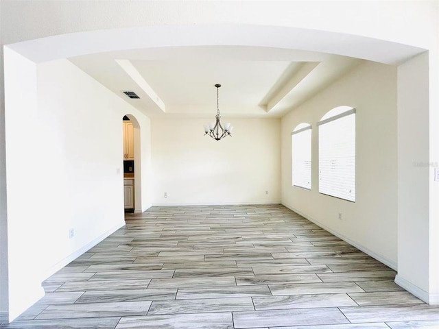 empty room featuring a raised ceiling and a notable chandelier