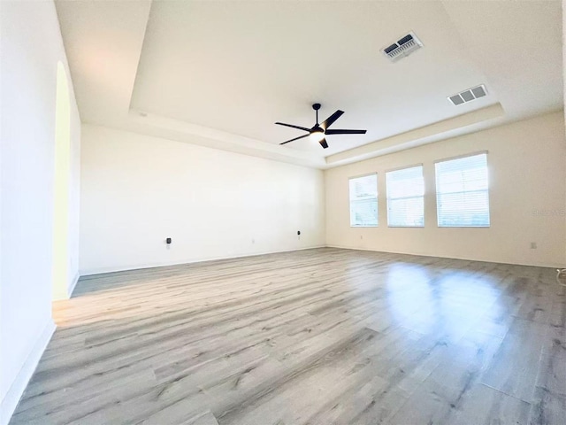 spare room with light wood-type flooring, a tray ceiling, and ceiling fan