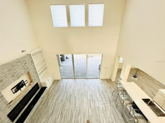 unfurnished living room featuring a stone fireplace, a towering ceiling, and light wood-type flooring