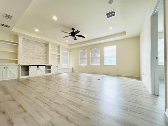 unfurnished living room with built in shelves, ceiling fan, a raised ceiling, and light hardwood / wood-style floors