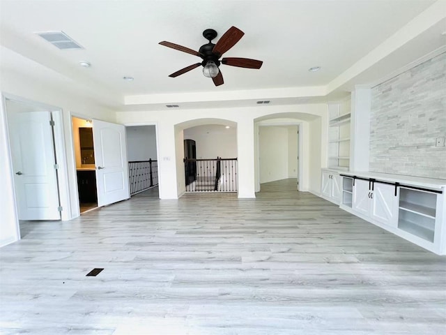 unfurnished living room featuring built in shelves, ceiling fan, and light wood-type flooring