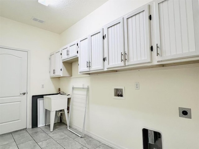 clothes washing area with cabinets, hookup for a washing machine, a textured ceiling, hookup for an electric dryer, and light tile patterned flooring