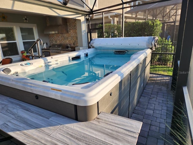 view of swimming pool featuring glass enclosure, grilling area, and a hot tub