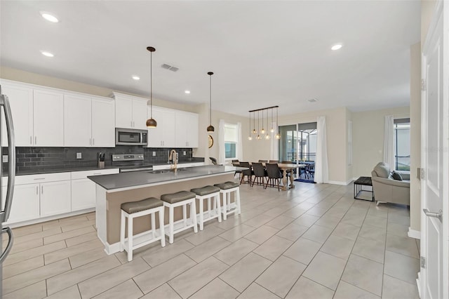 kitchen with appliances with stainless steel finishes, decorative light fixtures, an island with sink, sink, and backsplash