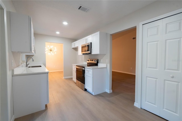 kitchen with white cabinetry, sink, stainless steel appliances, a notable chandelier, and light hardwood / wood-style floors