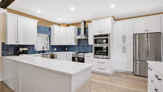 kitchen with white cabinets, appliances with stainless steel finishes, sink, and wall chimney range hood