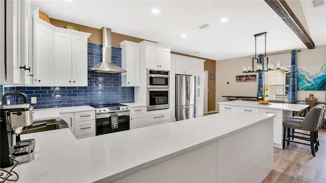 kitchen with appliances with stainless steel finishes, wall chimney range hood, beamed ceiling, white cabinetry, and hanging light fixtures