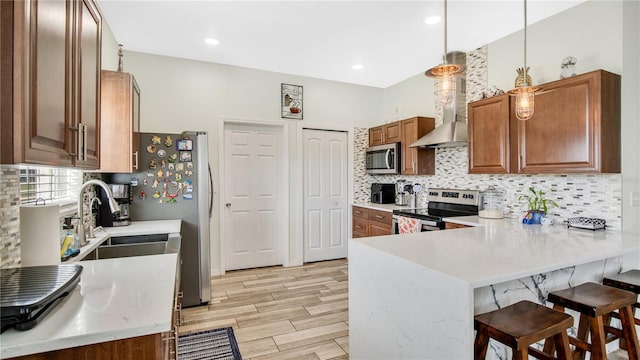 kitchen with hanging light fixtures, stainless steel appliances, wall chimney range hood, backsplash, and kitchen peninsula