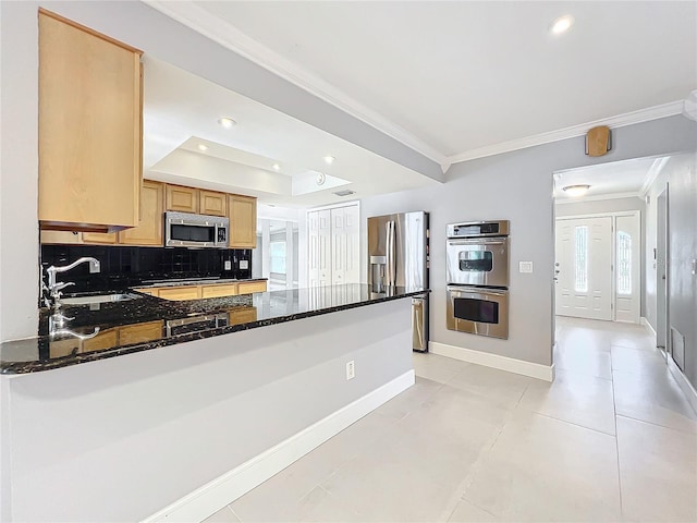 kitchen with stainless steel appliances, ornamental molding, a sink, dark stone countertops, and a peninsula