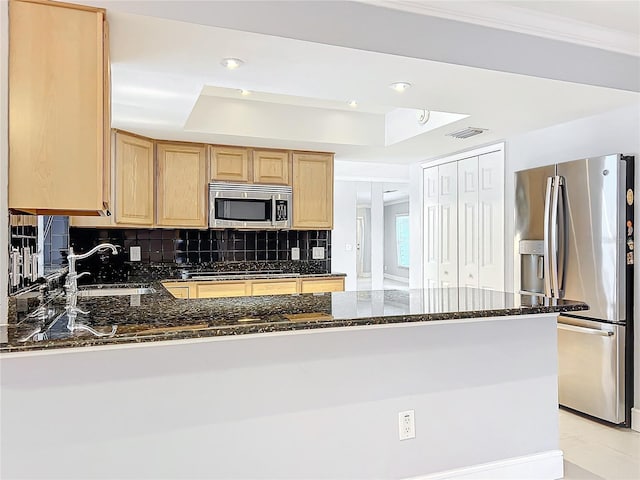 kitchen featuring stainless steel appliances, a peninsula, a sink, a tray ceiling, and dark stone countertops