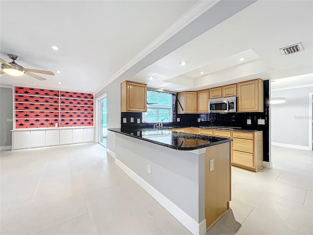 kitchen featuring a peninsula, a sink, visible vents, stainless steel microwave, and dark stone countertops