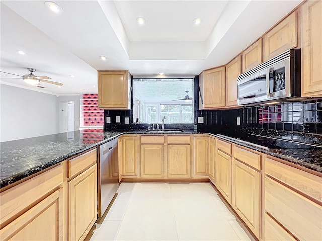 kitchen with decorative backsplash, appliances with stainless steel finishes, light brown cabinets, a sink, and dark stone counters