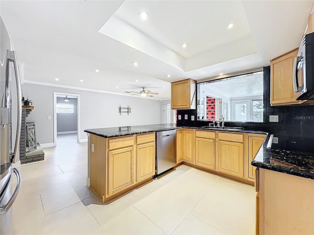 kitchen with a raised ceiling, dark stone counters, appliances with stainless steel finishes, a peninsula, and a sink