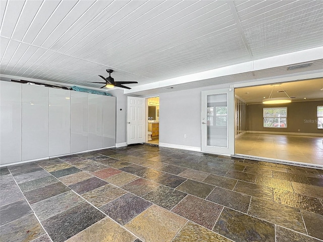 interior space with ceiling fan, stone tile flooring, and baseboards