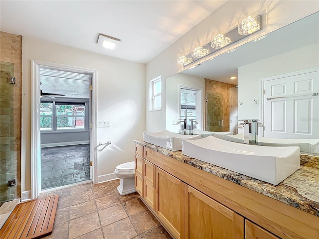 full bathroom with a sink, baseboards, double vanity, a stall shower, and stone tile flooring