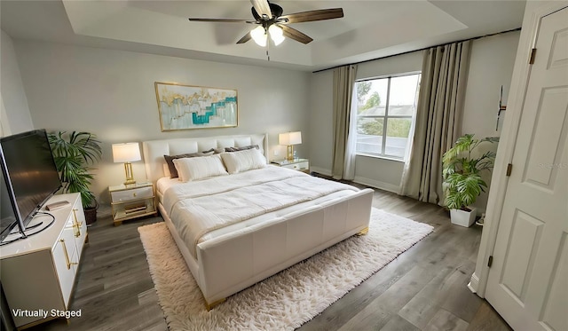 bedroom featuring hardwood / wood-style flooring, a raised ceiling, and ceiling fan