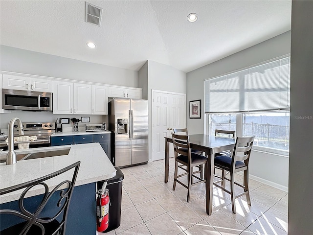 kitchen featuring sink, a textured ceiling, appliances with stainless steel finishes, light tile patterned flooring, and white cabinetry