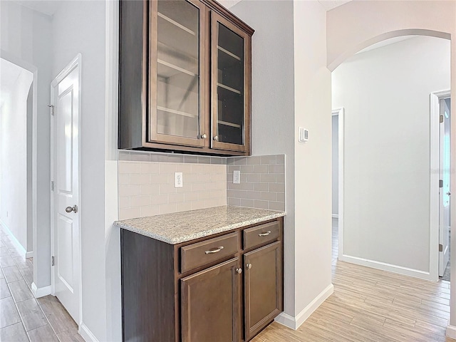 kitchen featuring dark brown cabinets, light stone counters, and decorative backsplash