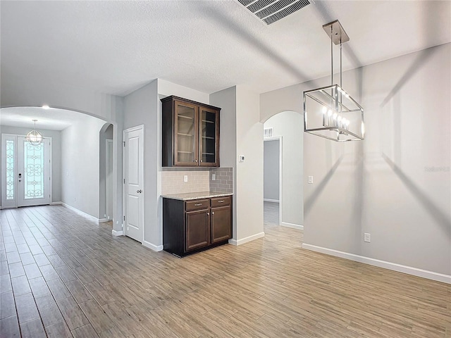 kitchen with hanging light fixtures, dark brown cabinets, light wood-type flooring, and tasteful backsplash