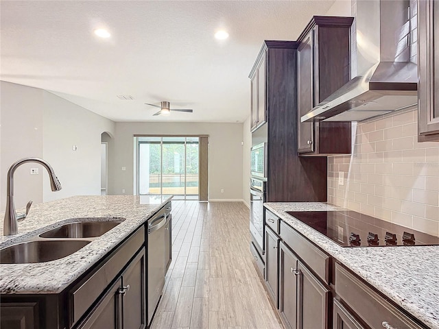 kitchen with sink, light stone counters, wall chimney exhaust hood, light hardwood / wood-style floors, and appliances with stainless steel finishes