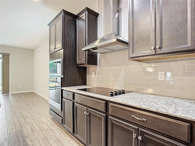 kitchen with light stone counters, wall chimney exhaust hood, light hardwood / wood-style floors, appliances with stainless steel finishes, and dark brown cabinetry