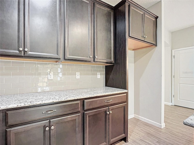 kitchen featuring light hardwood / wood-style flooring, dark brown cabinets, light stone counters, and decorative backsplash