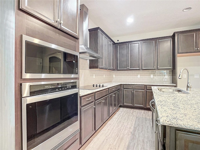 kitchen with light stone countertops, wall chimney range hood, decorative backsplash, appliances with stainless steel finishes, and sink