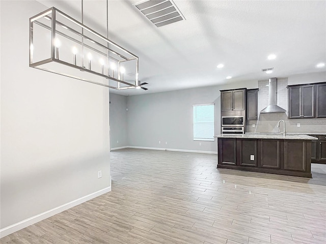 kitchen with hanging light fixtures, stainless steel appliances, dark brown cabinets, wall chimney exhaust hood, and light hardwood / wood-style flooring