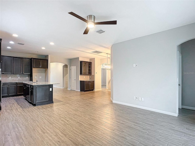 kitchen with light hardwood / wood-style flooring, a center island with sink, backsplash, ceiling fan, and sink