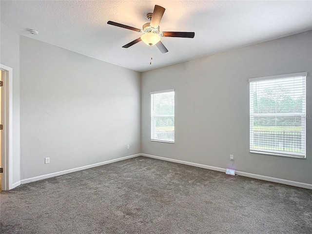 empty room featuring a healthy amount of sunlight, ceiling fan, a textured ceiling, and dark colored carpet