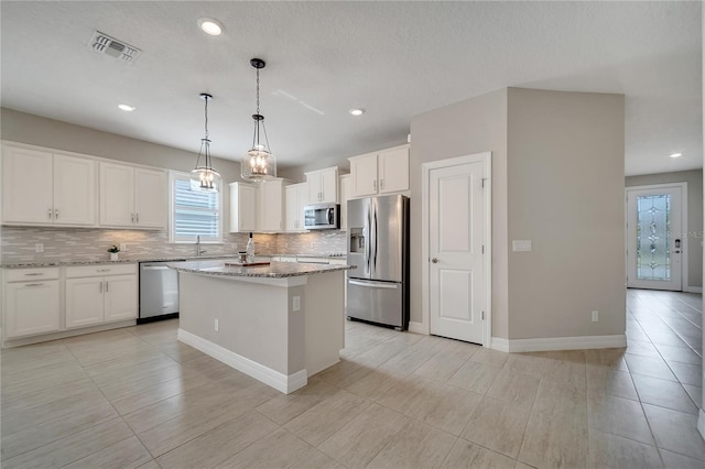 kitchen featuring a kitchen island, hanging light fixtures, appliances with stainless steel finishes, white cabinets, and light stone counters