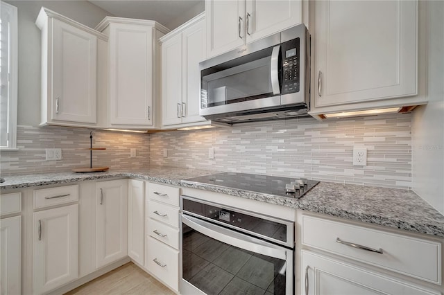 kitchen with light stone counters, backsplash, white cabinetry, and appliances with stainless steel finishes