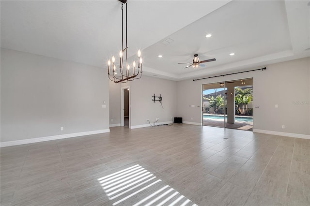 unfurnished living room featuring a raised ceiling and ceiling fan with notable chandelier