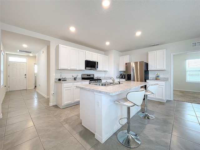 kitchen featuring a breakfast bar, a kitchen island with sink, sink, white cabinetry, and stainless steel appliances