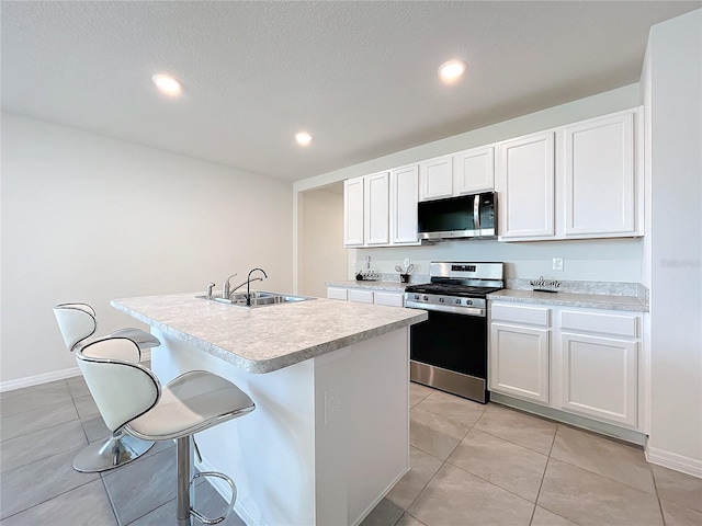 kitchen with a center island with sink, sink, light tile patterned floors, white cabinetry, and stainless steel appliances