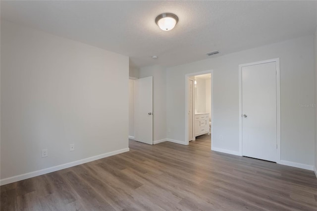 unfurnished bedroom featuring a closet, wood-type flooring, a textured ceiling, and ensuite bath