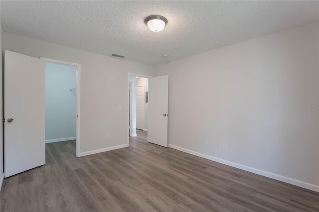 unfurnished bedroom featuring a textured ceiling, a walk in closet, a closet, and hardwood / wood-style floors