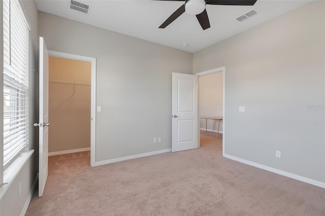 unfurnished bedroom with a spacious closet, a closet, ceiling fan, and light colored carpet