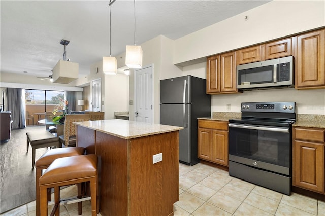 kitchen with a center island, hanging light fixtures, ceiling fan, appliances with stainless steel finishes, and light stone counters