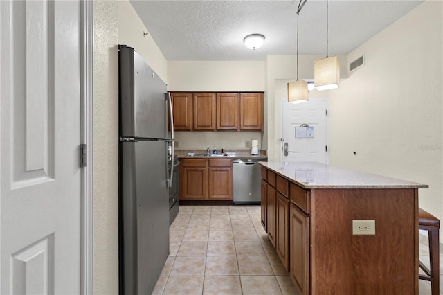 kitchen featuring light stone counters, a breakfast bar, a textured ceiling, stainless steel appliances, and hanging light fixtures