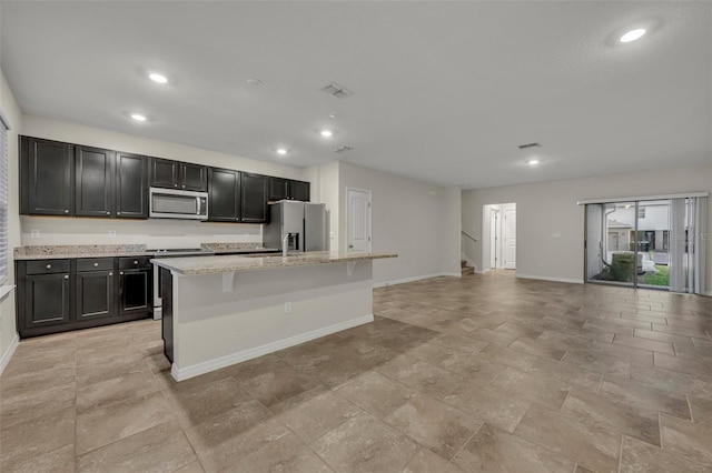 kitchen featuring light stone countertops, a kitchen island with sink, a breakfast bar area, and stainless steel appliances