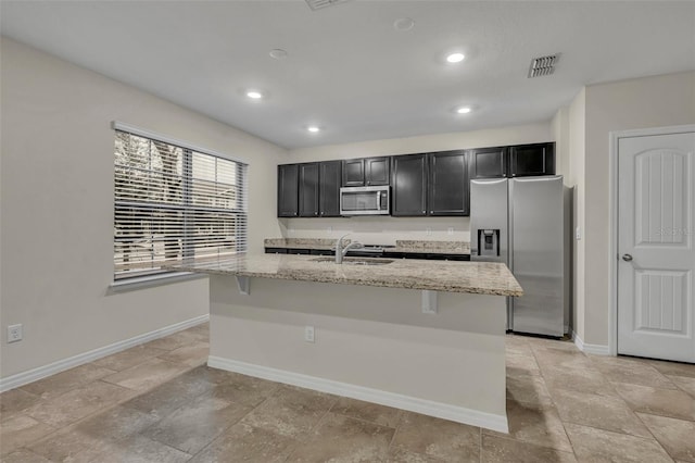 kitchen featuring appliances with stainless steel finishes, sink, light stone counters, and an island with sink