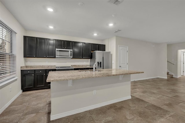 kitchen featuring a center island with sink, light stone counters, sink, and appliances with stainless steel finishes