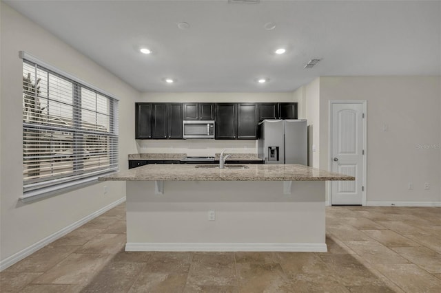 kitchen featuring light stone countertops, appliances with stainless steel finishes, a center island with sink, and sink